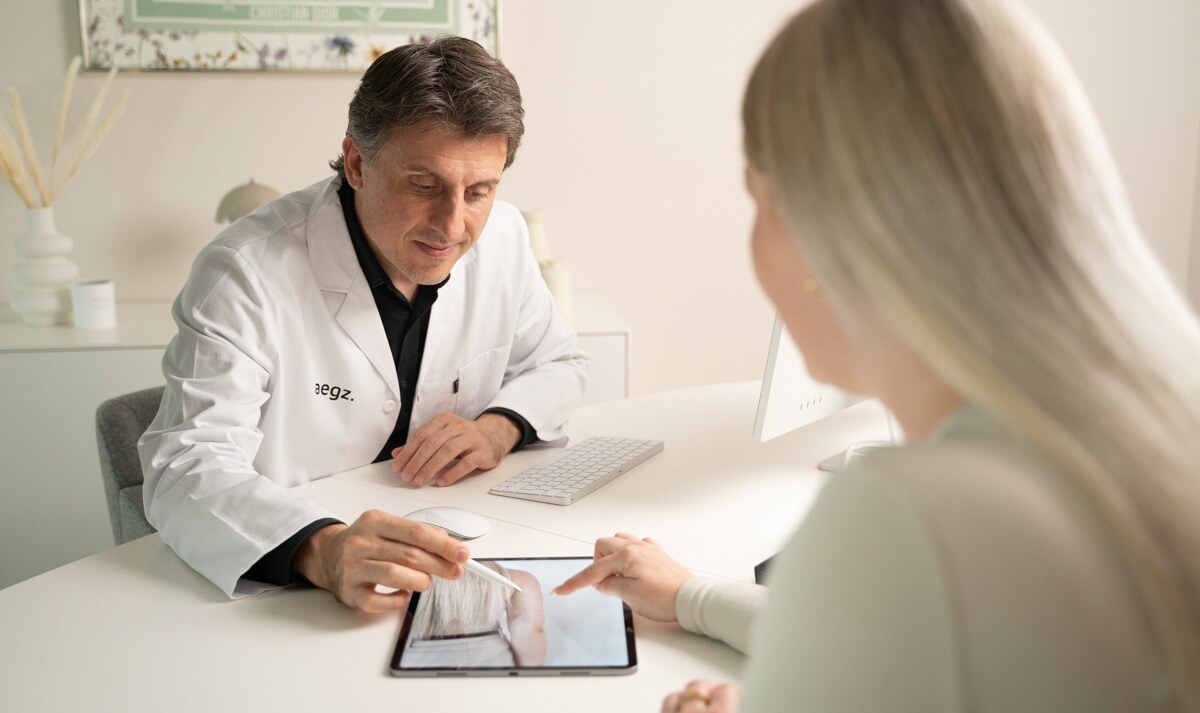 Dr. (TU) Ercan Cakmak im Beratungsgespräch zur Fettabsaugung an den Oberarmen mit einer Patientin – gemeinsamer Blick auf iPad-Bild der Behandlungsregion.